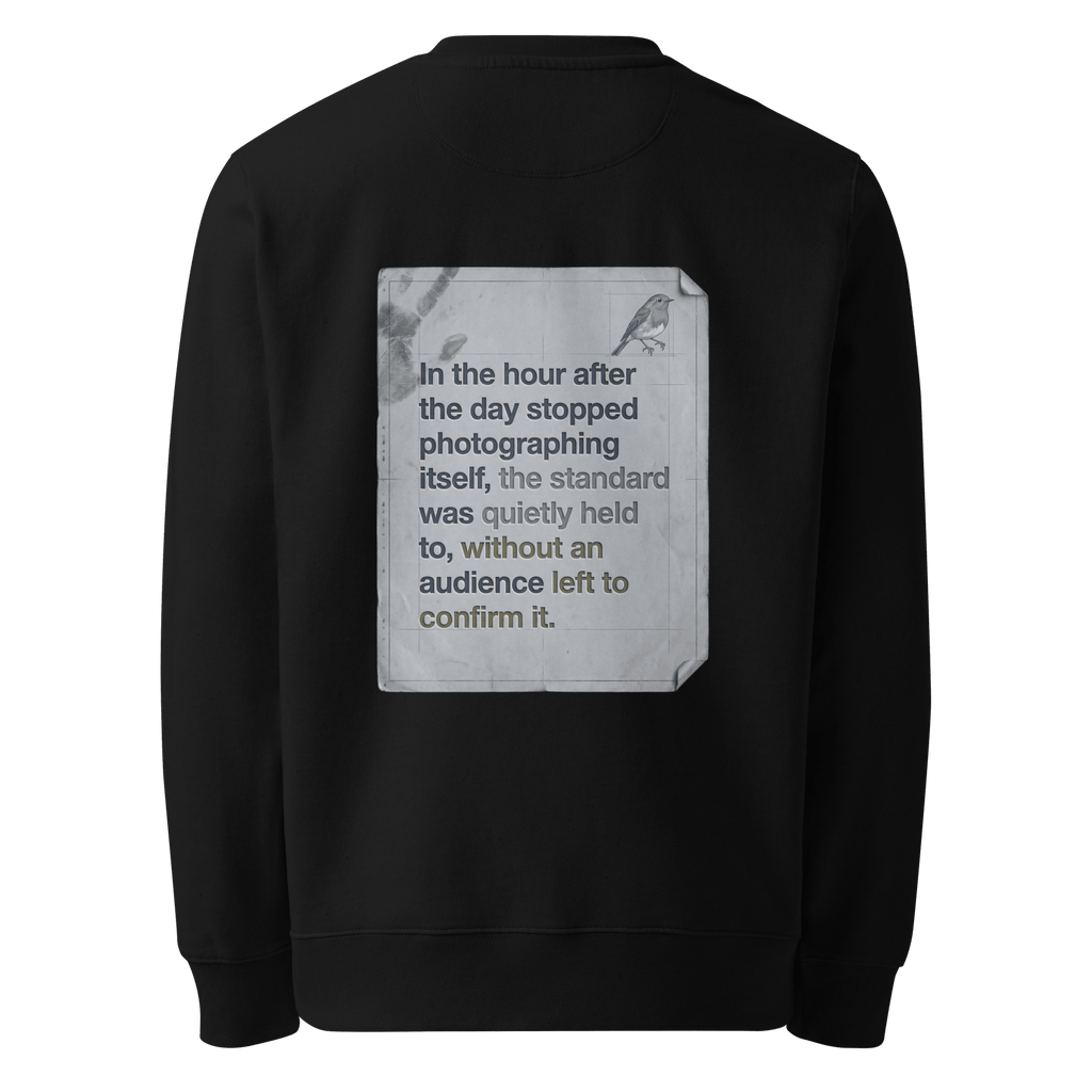 Quietly Held sweater, black — back view of torn paper slogan plate with robin, reading "In the hour after the day stopped photographing itself, the standard was quietly held to, without an audience left to confirm it." — Ricki Robin