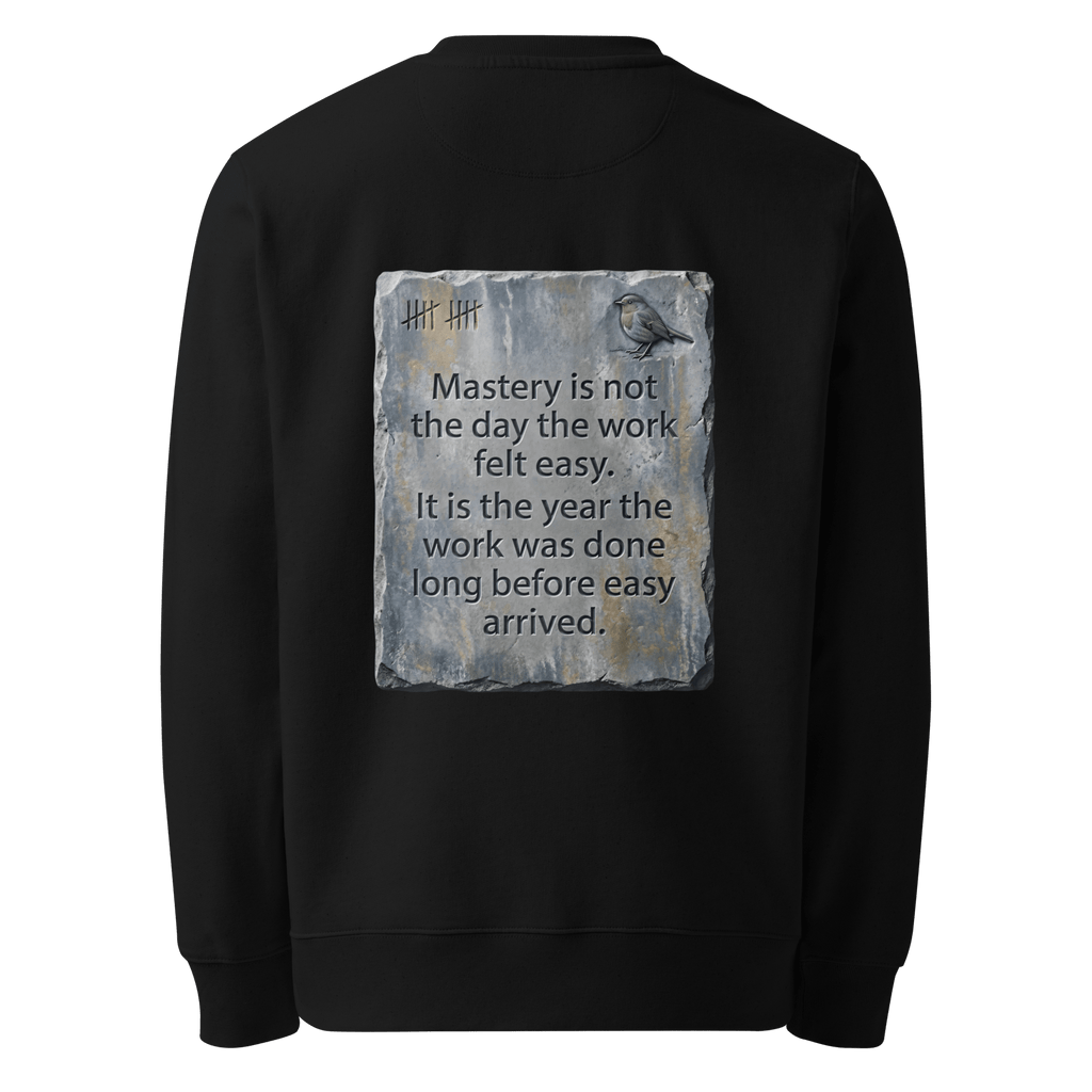 Long Before Easy sweater, black — back view of worn metal slogan plate with robin, reading "Mastery is not the day the work felt easy. It is the year the work was done long before easy arrived." — Ricki Robin