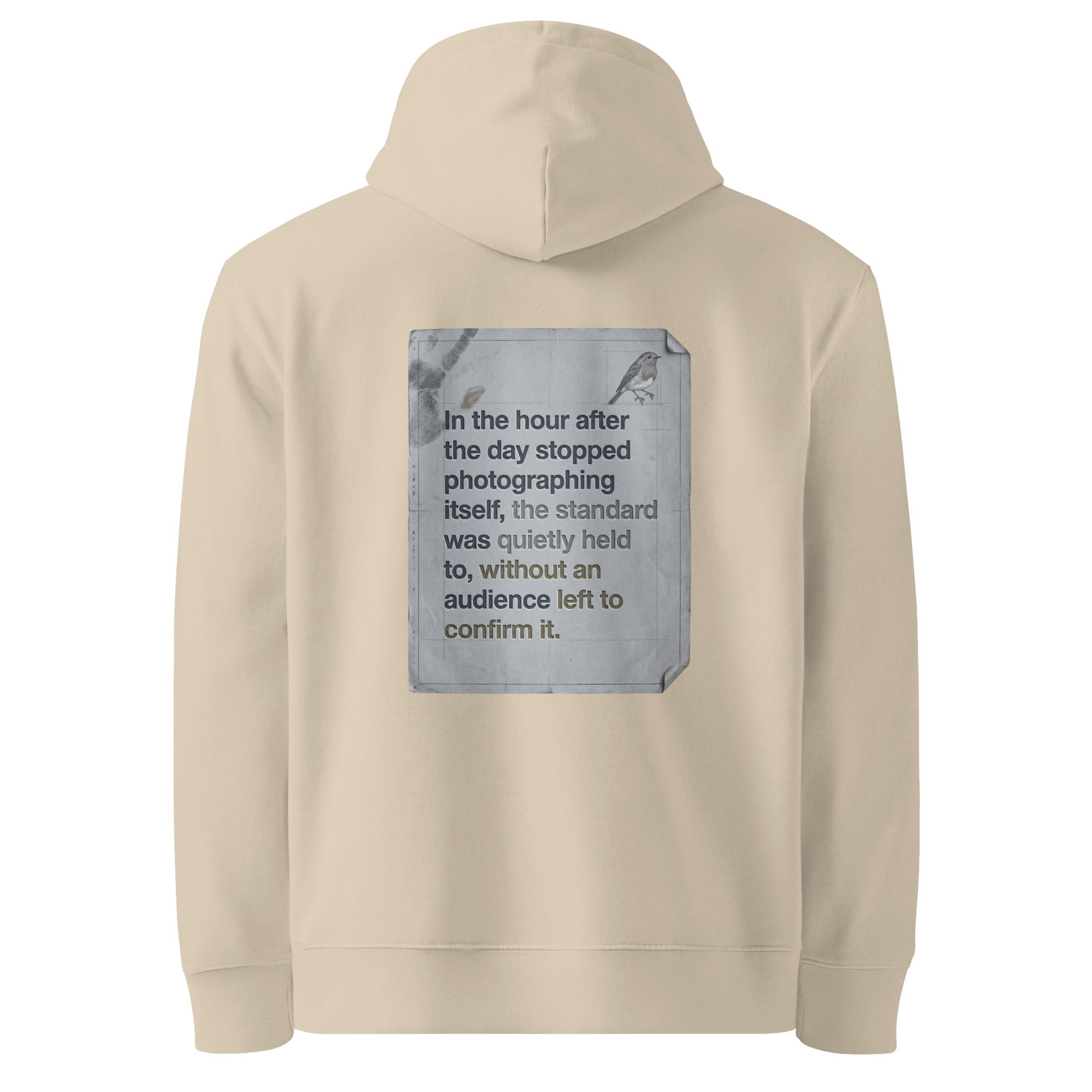 
Quietly Held hoodie, Desert Dust — back view of torn paper slogan plate with robin, reading "In the hour after the day stopped photographing itself, the standard was quietly held to, without an audience left to confirm it." — Ricki Robin